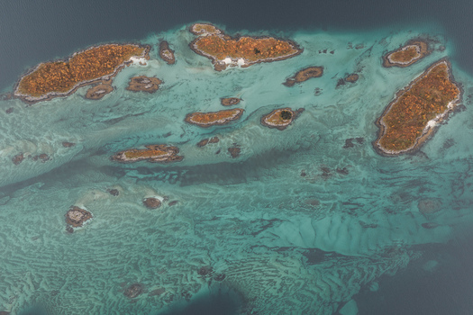 Aerial view of small islands with autumn colored vegetation surrounded by turquoise shallow waters and rocky seabed patterns in Senja Troms Norway.