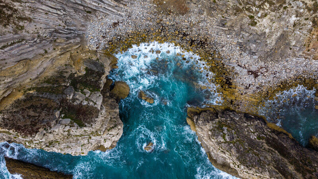 Aerial view of Lulworth Cove showing turquoise waters rocky cliffs and pebble beaches along the coastline in Wareham England United Kingdom. Aerial view of Lulworth Cove showing turquoise waters rocky cliffs and pebble beaches along the coastline in Wareham England United Kingdom.