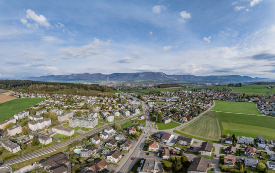 Aerial view of residential houses and green fields with the Jura mountains in the background under a blue sky in Biberist Solothurn Switzerland. Aerial view of residential houses and green fields with the Jura mountains in the background under a blue sky in Biberist Solothurn Switzerland.