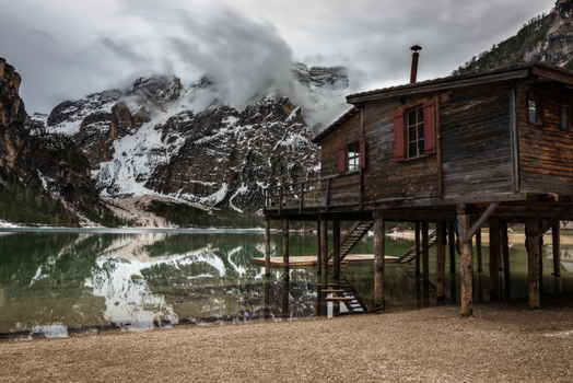 View of the iconic wooden boathouse on stilts at Lake Braies with snow capped Dolomites peaks reflected in the calm water under a cloudy sky Trentino Alto Adige Italy. View of the iconic wooden boathouse on stilts at Lake Braies with snow capped Dolomites peaks reflected in the calm water under a cloudy sky Trentino Alto Adige Italy.