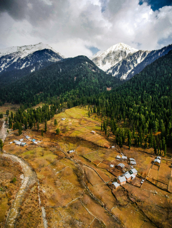Aerial view of the valley in Pahalgam featuring small village houses a winding river and lush pine forests set against snow capped mountains in Pahalgam Kashmir India.