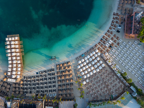 Aerial view of Ksamil beach featuring rows of sun loungers and umbrellas turquoise water and a wooden pier in Ksamil Vlore County Albania. Aerial view of Ksamil beach featuring rows of sun loungers and umbrellas turquoise water and a wooden pier in Ksamil Vlore County Albania.