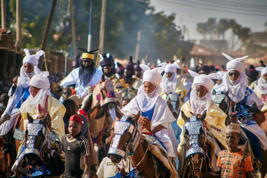 Zaria city Nigeria 21 March 2026 View of a vibrant procession of riders in white and blue attire on adorned horses through a dusty street. Zaria city Nigeria 21 March 2026 View of a vibrant procession of riders in white and blue attire on adorned horses through a dusty street.