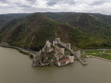 Aerial view of Golubac Fortress situated on a rocky cliff overlooking the Danube River surrounded by lush green hills and a cloudy sky in Golubac Branicevski okrug Serbia. Aerial view of Golubac Fortress situated on a rocky cliff overlooking the Danube River surrounded by lush green hills and a cloudy sky in Golubac Branicevski okrug Serbia.