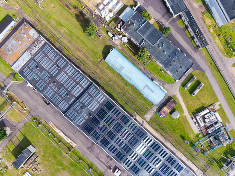 Aerial view of an industrial facility featuring extensive solar panel arrays on the roof surrounded by green fields railway tracks and storage tanks in Olaine Olaine Municipality Latvia. Aerial view of an industrial facility featuring extensive solar panel arrays on the roof surrounded by green fields railway tracks and storage tanks in Olaine Olaine Municipality Latvia.