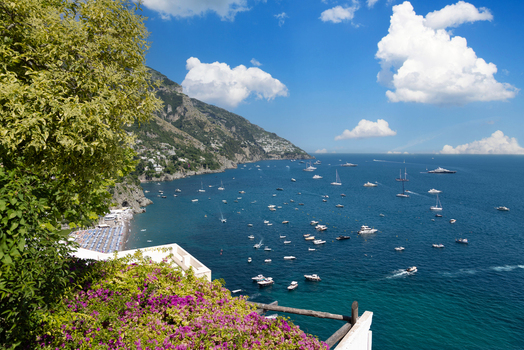 Aerial view of Positano with colorful cliffside buildings numerous boats on the blue sea and vibrant flowers in the foreground in Positano Campania Italy. Aerial view of Positano with colorful cliffside buildings numerous boats on the blue sea and vibrant flowers in the foreground in Positano Campania Italy.