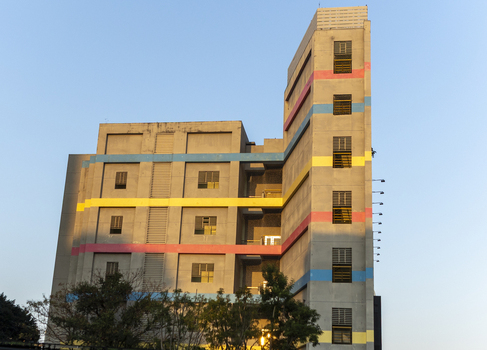 View of a modern concrete building featuring vibrant horizontal stripes of blue yellow and pink under a clear sky with green trees in the foreground Taipei City Taiwan. View of a modern concrete building featuring vibrant horizontal stripes of blue yellow and pink under a clear sky with green trees in the foreground Taipei City Taiwan.