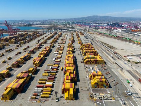 Aerial view of the Port of Long Beach featuring rows of colorful shipping containers industrial cranes and railway tracks under a clear blue sky in Long Beach California United States. Aerial view of the Port of Long Beach featuring rows of colorful shipping containers industrial cranes and railway tracks under a clear blue sky in Long Beach California United States.