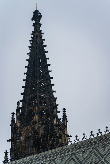 View of the intricate gothic spire of St. Vitus Cathedral with its detailed stone carvings and tiled roof against a cloudy sky in Prague Prague Czechia.
