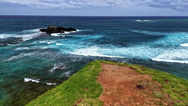Aerial view of grassy cliff overlooking ocean waves Indonesia.