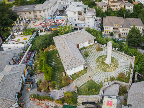 Aerial view of a traditional stone roofed building and a circular paved courtyard with a monument in the historic old town of Gjirokaster Gjirokaster County Albania. Aerial view of a traditional stone roofed building and a circular paved courtyard with a monument in the historic old town of Gjirokaster Gjirokaster County Albania.
