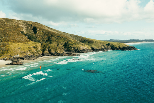 Aerial view of Puwheke Beach with a kite surfer gliding over turquoise ocean waves near rugged green hills on the Karikari Peninsula Northland Region New Zealand. Aerial view of Puwheke Beach with a kite surfer gliding over turquoise ocean waves near rugged green hills on the Karikari Peninsula Northland Region New Zealand.