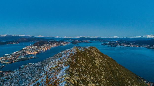 Aerial view of the town of Alesund nestled between fjords and mountains at twilight with snow dusted peaks and city lights reflecting on the water in Alesund More og Romsdal Norway. Aerial view of the town of Alesund nestled between fjords and mountains at twilight with snow dusted peaks and city lights reflecting on the water in Alesund More og Romsdal Norway.