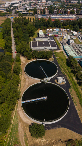 Aerial view of a wastewater treatment plant featuring large circular sedimentation tanks surrounded by lush trees and industrial infrastructure in Milan Lombardy Italy. Aerial view of a wastewater treatment plant featuring large circular sedimentation tanks surrounded by lush trees and industrial infrastructure in Milan Lombardy Italy.