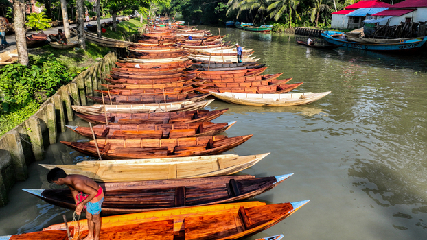 Aerial view of a long line of wooden boats their prows gleaming under the sun moored along the canal s edge Pirojpur Pourashava Barisal Division Bangladesh. Aerial view of a long line of wooden boats their prows gleaming under the sun moored along the canal s edge Pirojpur Pourashava Barisal Division Bangladesh.