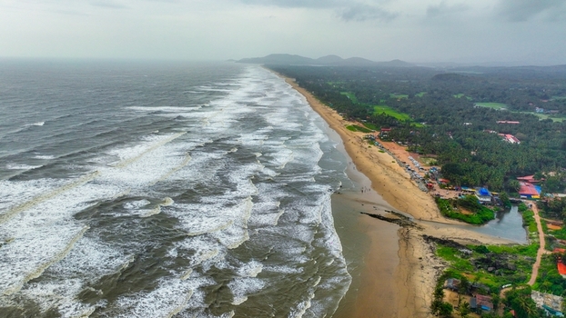 Aerial view of Gokarna Main Beach with crashing waves sandy coastline lush palm trees and coastal vegetation in Gokarna Karnataka India.