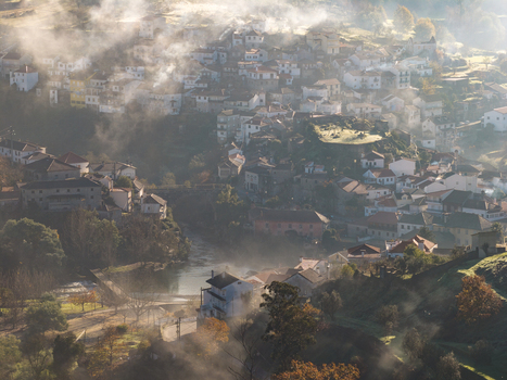 Aerial view of the historic village of Avo shrouded in morning mist with traditional white houses and a river flowing through the valley Oliveira do Hospital Coimbra District Portugal.