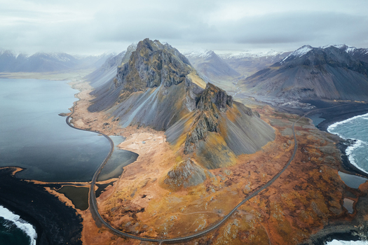 Aerial view of the jagged peaks of Eystrahorn mountain and the black sand beach of Hvalnes Nature Reserve with a winding road Eystrahorn Sveitarfelagid Hornafjordur Iceland. Aerial view of the jagged peaks of Eystrahorn mountain and the black sand beach of Hvalnes Nature Reserve with a winding road Eystrahorn Sveitarfelagid Hornafjordur Iceland.
