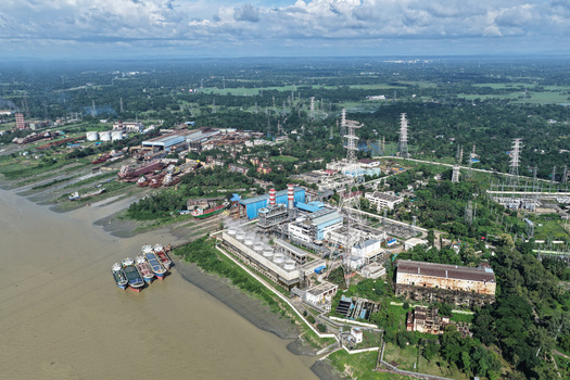 Aerial view of the Karnaphuli River with a power plant industrial facilities cargo ships moored along the muddy banks and lush greenery in Chattogram Chattogram Division Bangladesh.