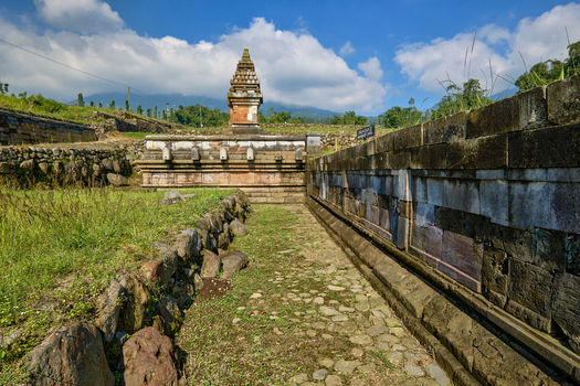 View of the ancient Situs Liyangan archaeological site featuring stone temple structures and terraces under a blue sky in Temanggung Central Java Indonesia.