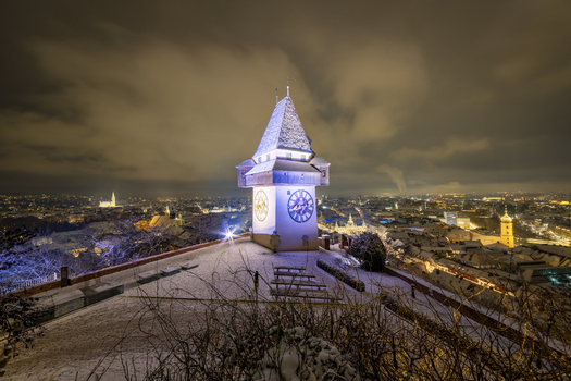 View of the clock tower at night a beacon of light amidst the snowy landscape illuminating the cityscape below Graz Styria Austria. View of the clock tower at night a beacon of light amidst the snowy landscape illuminating the cityscape below Graz Styria Austria.