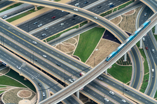 View of a complex multi level highway interchange with a blue metro train and cars driving on ramps surrounded by green landscaping in Dubai Dubai United Arab Emirates. View of a complex multi level highway interchange with a blue metro train and cars driving on ramps surrounded by green landscaping in Dubai Dubai United Arab Emirates.
