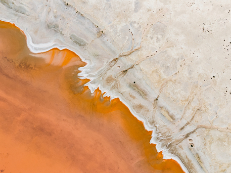 Aerial view of an abstract salt lake in the Mallee region featuring vibrant orange water contrasting with white salt crust and dry earth patterns in Woorinen North Victoria Australia. Aerial view of an abstract salt lake in the Mallee region featuring vibrant orange water contrasting with white salt crust and dry earth patterns in Woorinen North Victoria Australia.