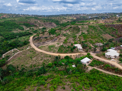 Aerial view of winding dirt roads cutting through verdant and cleared hillsides dotted with a few light roofed homes under a cloudy sky Asaga Abia Nigeria. Aerial view of winding dirt roads cutting through verdant and cleared hillsides dotted with a few light roofed homes under a cloudy sky Asaga Abia Nigeria.