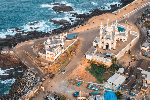 Aerial view of the Vizhinjam Juma Masjid along the rocky coastline featuring white minarets domes coastal roads and the blue waters of the Arabian Sea in Kovalam Keralam India. Aerial view of the Vizhinjam Juma Masjid along the rocky coastline featuring white minarets domes coastal roads and the blue waters of the Arabian Sea in Kovalam Keralam India.