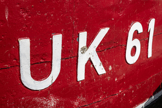 View of the white registration number UK 61 on the weathered red hull of a traditional fishing boat at Urk Harbour in Urk Flevoland Netherlands.