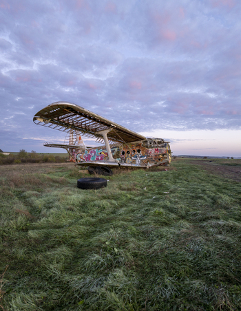Aerial view of an abandoned graffiti covered biplane resting in a grassy field under a soft twilight sky in Bulgaria. Aerial view of an abandoned graffiti covered biplane resting in a grassy field under a soft twilight sky in Bulgaria.