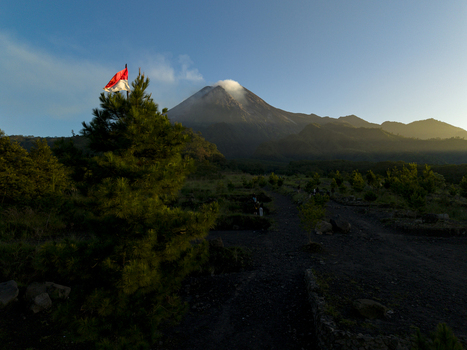 Aerial view of Bunker Kaliadem Merapi with the smoking Mount Merapi volcano an Indonesian flag on a tree and lush greenery in Kecamatan Pakem Daerah Istimewa Yogya Indonesia. Aerial view of Bunker Kaliadem Merapi with the smoking Mount Merapi volcano an Indonesian flag on a tree and lush greenery in Kecamatan Pakem Daerah Istimewa Yogya Indonesia.