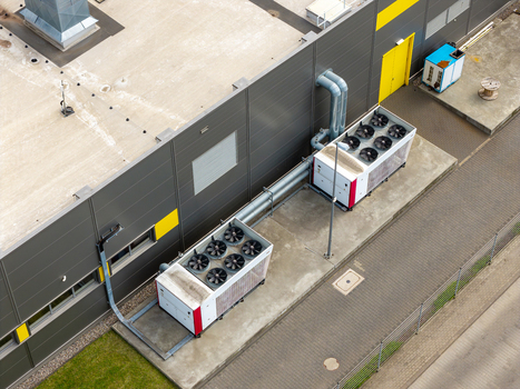 Aerial view of industrial cooling units with large fans installed on the concrete ground next to a modern logistics center building in Warsaw Masovian Voivodeship Poland. Aerial view of industrial cooling units with large fans installed on the concrete ground next to a modern logistics center building in Warsaw Masovian Voivodeship Poland.