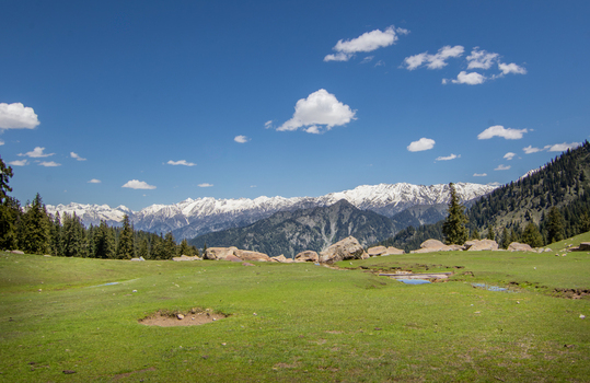 View of the meadow landscape near Jahaz Banda Alpine Rest House with snow capped mountains in the background under a clear blue sky in Kumrat Valley Khyber Pakhtunkhwa Pakistan. View of the meadow landscape near Jahaz Banda Alpine Rest House with snow capped mountains in the background under a clear blue sky in Kumrat Valley Khyber Pakhtunkhwa Pakistan.