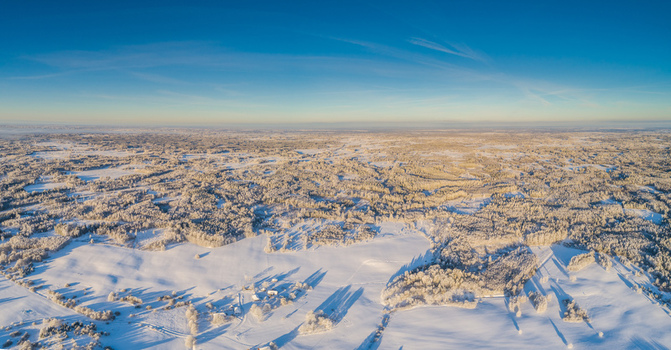 Aerial view of a vast snow covered landscape featuring dense forests and open fields under a clear blue sky during the golden hour in Latvia. Aerial view of a vast snow covered landscape featuring dense forests and open fields under a clear blue sky during the golden hour in Latvia.
