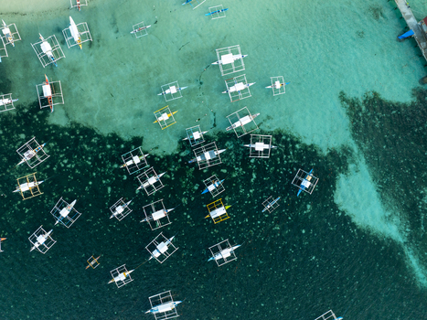 Aerial view of traditional outrigger boats floating in the turquoise waters surrounding Naked Island with coral reefs visible beneath the surface in Siargao Philippines. Aerial view of traditional outrigger boats floating in the turquoise waters surrounding Naked Island with coral reefs visible beneath the surface in Siargao Philippines.