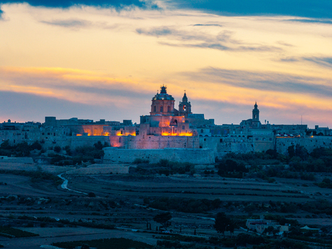 Aerial view of the historic fortified city of Mdina with its illuminated cathedral and ancient stone walls set against a vibrant sunset sky in Mdina Western Region Malta. Aerial view of the historic fortified city of Mdina with its illuminated cathedral and ancient stone walls set against a vibrant sunset sky in Mdina Western Region Malta.