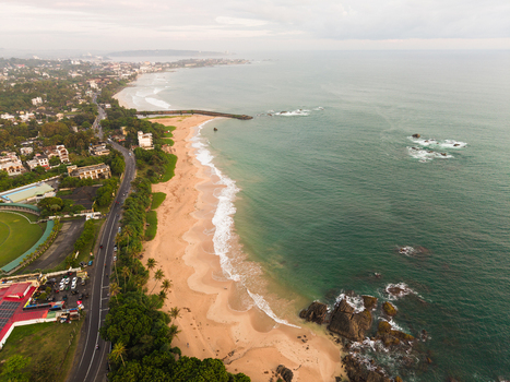 Aerial view of the sandy coastline with waves crashing on the shore a coastal road and lush tropical greenery in Galle Southern Province Sri Lanka.