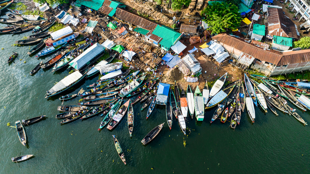 Rangamati Chittagong Division Bangladesh 19 October 2022 Aerial view of a busy riverbank market with numerous wooden boats docked along the shore surrounded by stalls and greenery.
