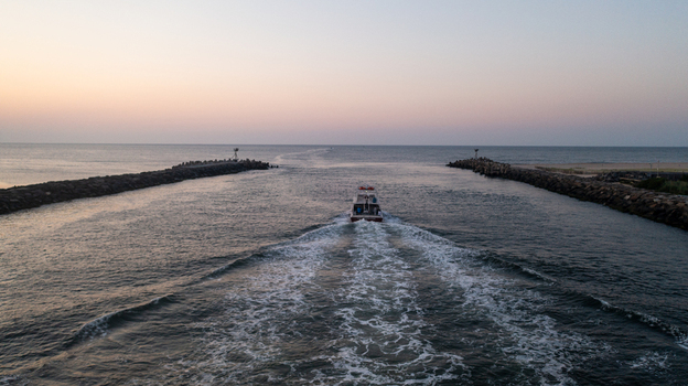 Aerial view of a boat leaving the Manasquan Beach inlet at sunset with stone jetties on both sides and a calm sea in Manasquan New Jersey United States. Aerial view of a boat leaving the Manasquan Beach inlet at sunset with stone jetties on both sides and a calm sea in Manasquan New Jersey United States.