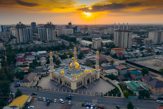 Aerial view of Mahmud Kashgari Mosque with its golden domes and tall minarets surrounded by the urban skyline under a vibrant sunset sky Bishkek Bishkek City Kyrgyzstan.