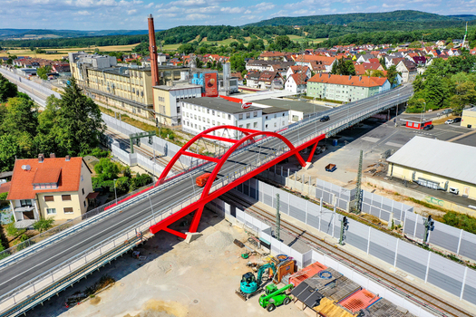 Aerial view of the red arched Piastenbrucke spanning over railway tracks near industrial buildings and residential houses in Forchheim Bayern Germany.