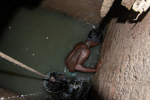 Dhaka Bangladesh 18 April 2018 View of a sewer cleaner working inside a narrow water filled pit with brick walls and a bucket on a rope. Dhaka Bangladesh 18 April 2018 View of a sewer cleaner working inside a narrow water filled pit with brick walls and a bucket on a rope.