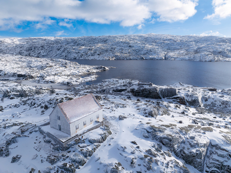 Aerial view of a solitary white building embraced by snow dusted rocks stands sentinel over the tranquil deep blue lake Lagoa Comprida São Romão Portugal. Aerial view of a solitary white building embraced by snow dusted rocks stands sentinel over the tranquil deep blue lake Lagoa Comprida São Romão Portugal.