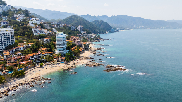 Aerial view of turquoise waters meeting the sandy shore lined with buildings climbing the lush green hillsides Puerto Vallarta Jalisco Mexico.