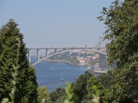 View of the Arrabida Bridge spanning the Douro River with urban buildings and lush trees in the foreground in Porto Porto District Portugal. View of the Arrabida Bridge spanning the Douro River with urban buildings and lush trees in the foreground in Porto Porto District Portugal.