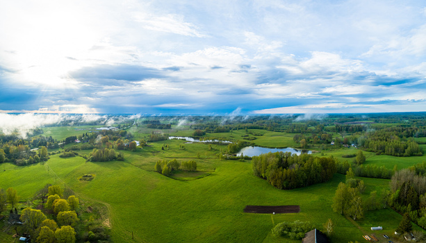 Aerial view of a lush green rural landscape featuring rolling fields small ponds scattered trees and a dramatic cloudy sky in Latvia. Aerial view of a lush green rural landscape featuring rolling fields small ponds scattered trees and a dramatic cloudy sky in Latvia.