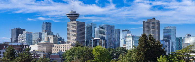Aerial view of the Vancouver Lookout tower and modern downtown skyline with lush green trees under a blue sky in Vancouver British Columbia Canada.
