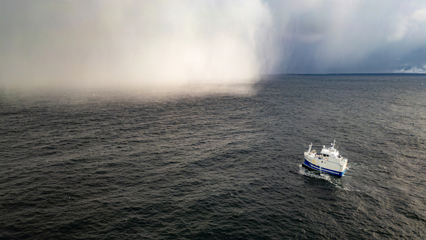 Aerial view of a small white and blue fishing boat navigating the dark waters of the Norwegian Sea near the coastal village of Reine Nordland Norway.