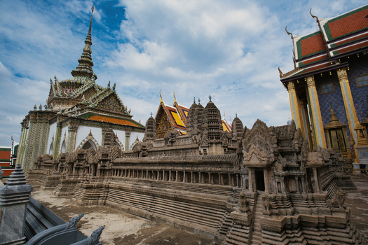 View of The Grand Palace featuring intricate stone models of Angkor Wat ornate temple architecture and traditional Thai roofs in Bangkok Thailand. View of The Grand Palace featuring intricate stone models of Angkor Wat ornate temple architecture and traditional Thai roofs in Bangkok Thailand.